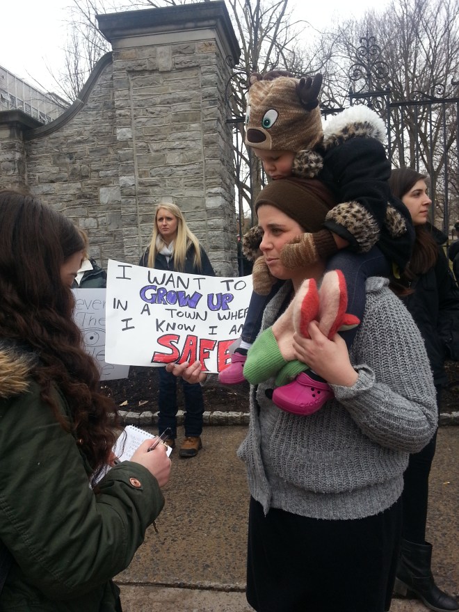 Picture of a toddler and her mother carrying a sign that says, "I want to grow up in a town what I know I am safe."