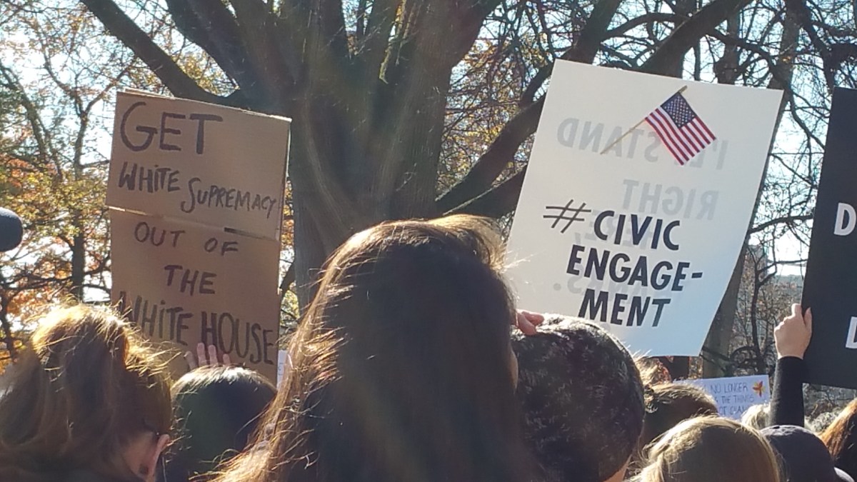picture of two signs. Once says "Get White Supremacy Out of the White House" and the other one has a flag with the hashtag "#CivicEngagement" printed underneath.