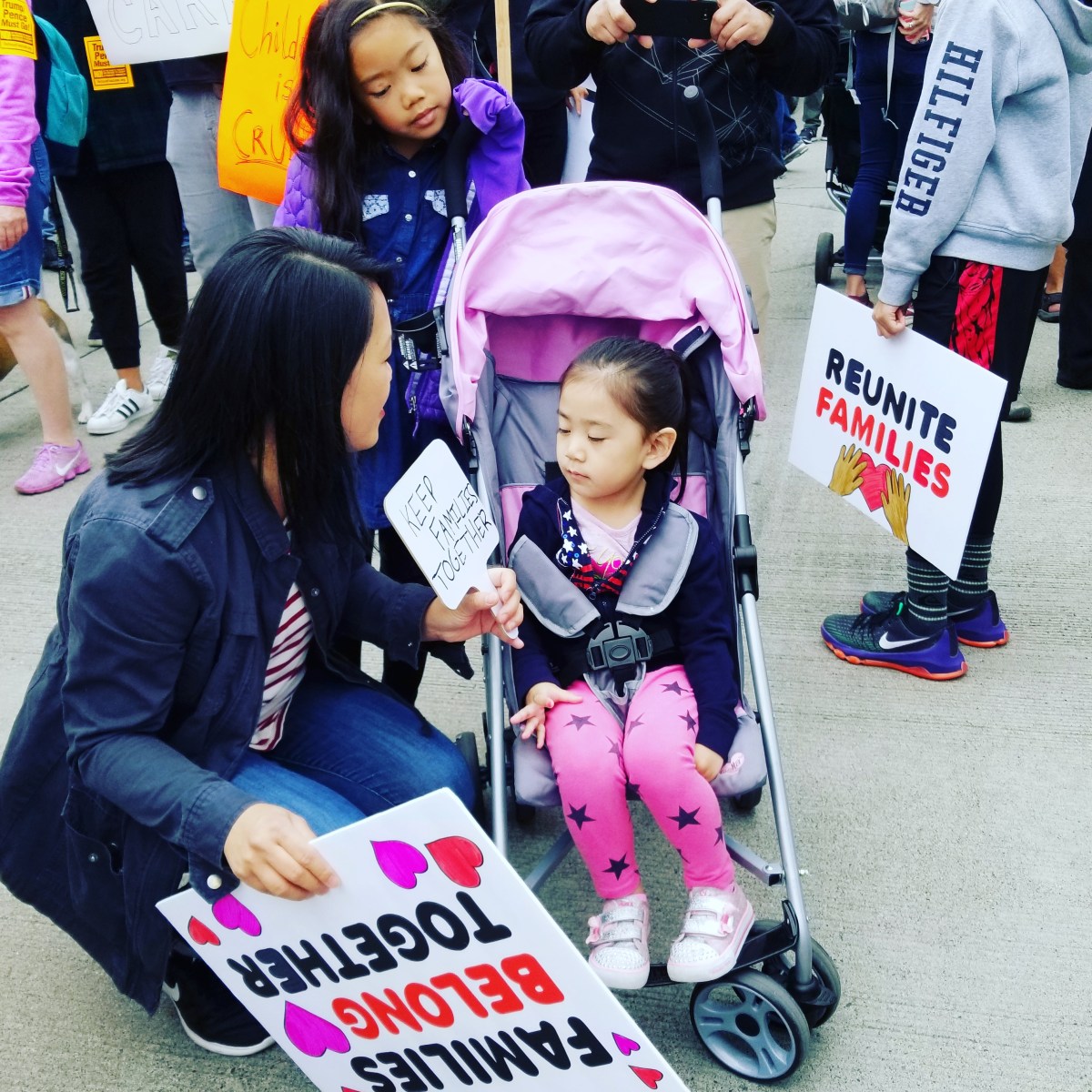 Picture of a girl sitting in a stroller with her mother and sister holding signs that say, "Families belong together."